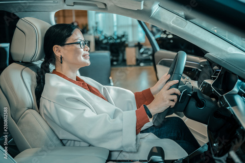 Woman sitting at the wheel in automobile showroom.