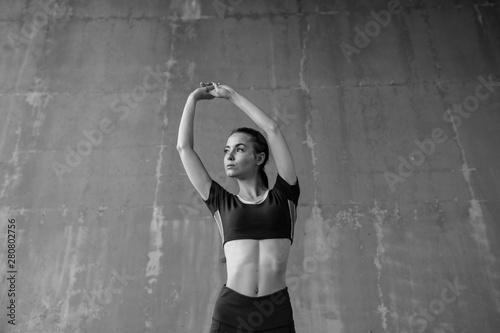 Sports woman on urban gray background. Fitness model working out outdoor. Beautiful slim brunette girl doing stretching warmup exercise. Black and white.
