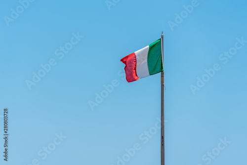 an Italian flag blowing in the wind against a bright blue sky