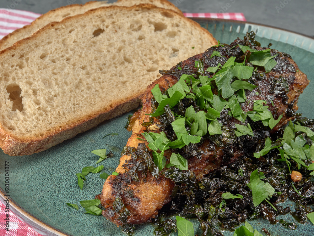 Fried sea bass with parsley.It's on a porcelain plate.On grey background Fried sea bass with parsley.It's on a porcelain plate.On grey background