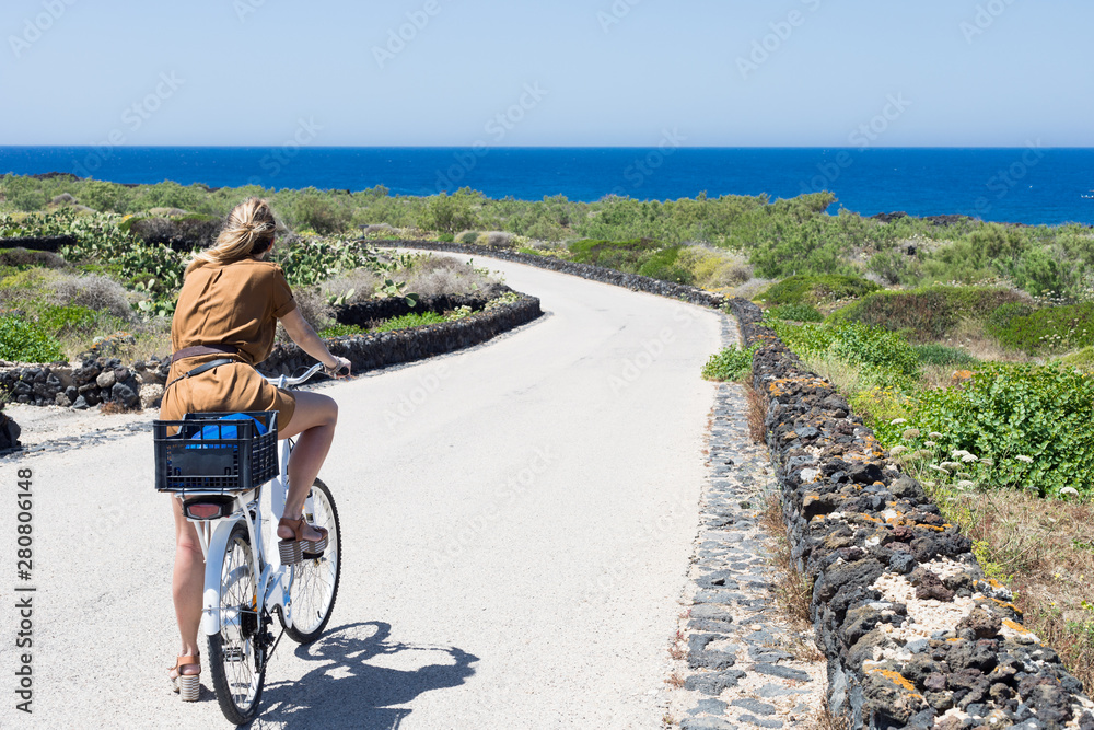Blonde girl riding bike near seaside on summer at Linosa Island near Lampedusa Island Sicily Italy 