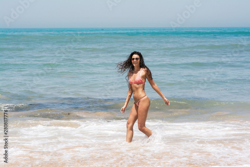 A young woman enjoying great time on the beach, walking in the waves of the seashore