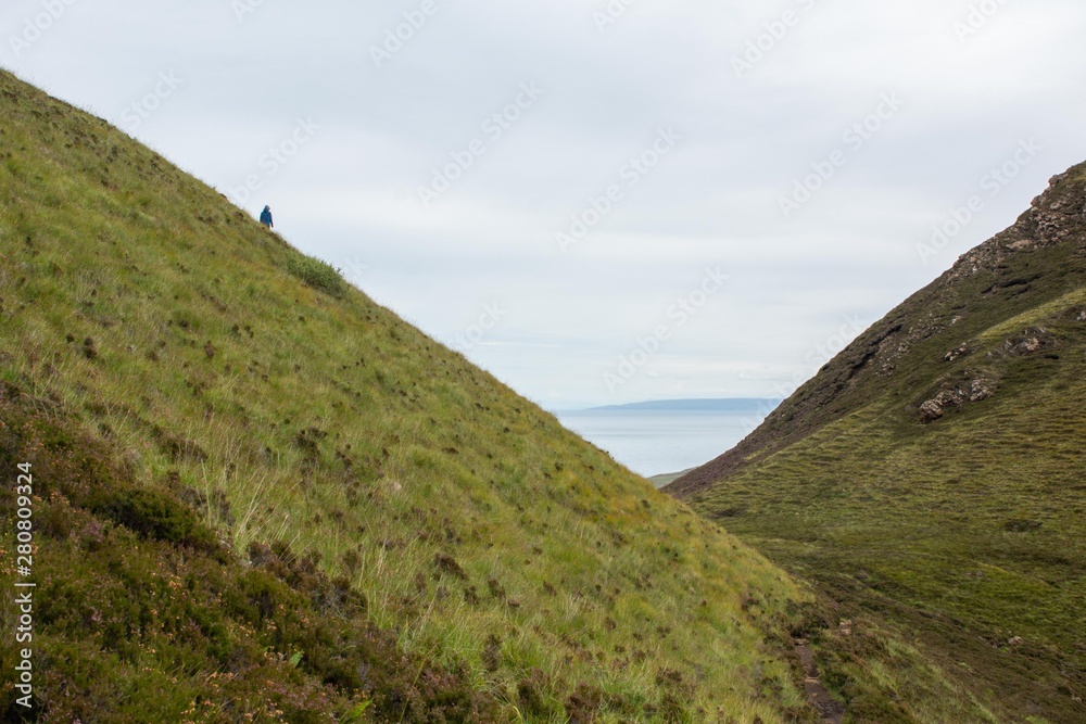 Person walking on a hill with ocean in the background