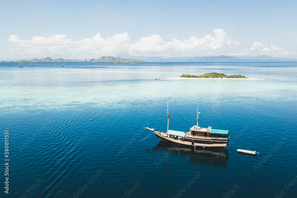 Luxury cruise boat sailing near coral reef atoll island with amazing white tropical beach and mountains on horizon. Aerial view. Luxury marine travel and vacations concept.