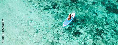 Woman sitting on sup board and enjoying turquoise transparent water and coral reef. Tropical travel, wanderlust and water activity concept.