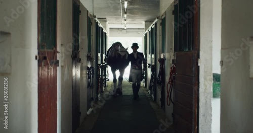 Cinematic slow motion of young horsemanship master dressed in a professional apparel is walking with his horse in stable before  a competition of racing and dressage on a riding hall. photo