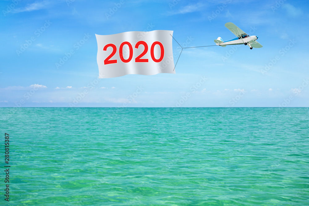 Happy new year 2020 written on banner pulling airplane on background of a sky and sea. Invitation on Merry Christmas and New Year. Happy new year 2020 written on banner pulling airplane on background of a sky and sea. Invitation on Merry Christmas and New Year.