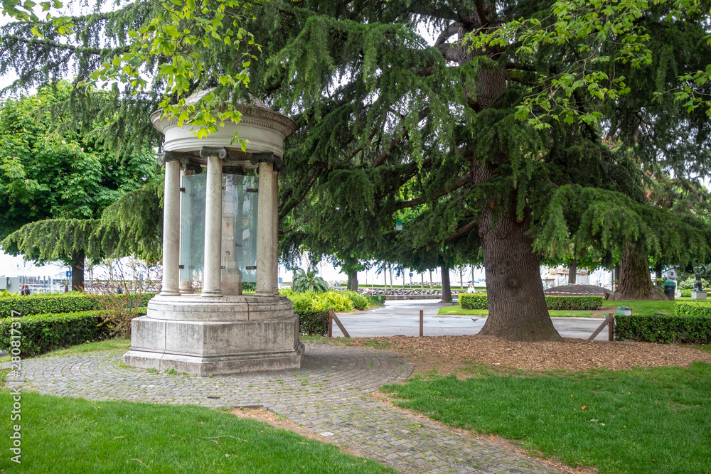 Beautiful old stone monument with big lush green tree in public park, Lausanne, Switzerland