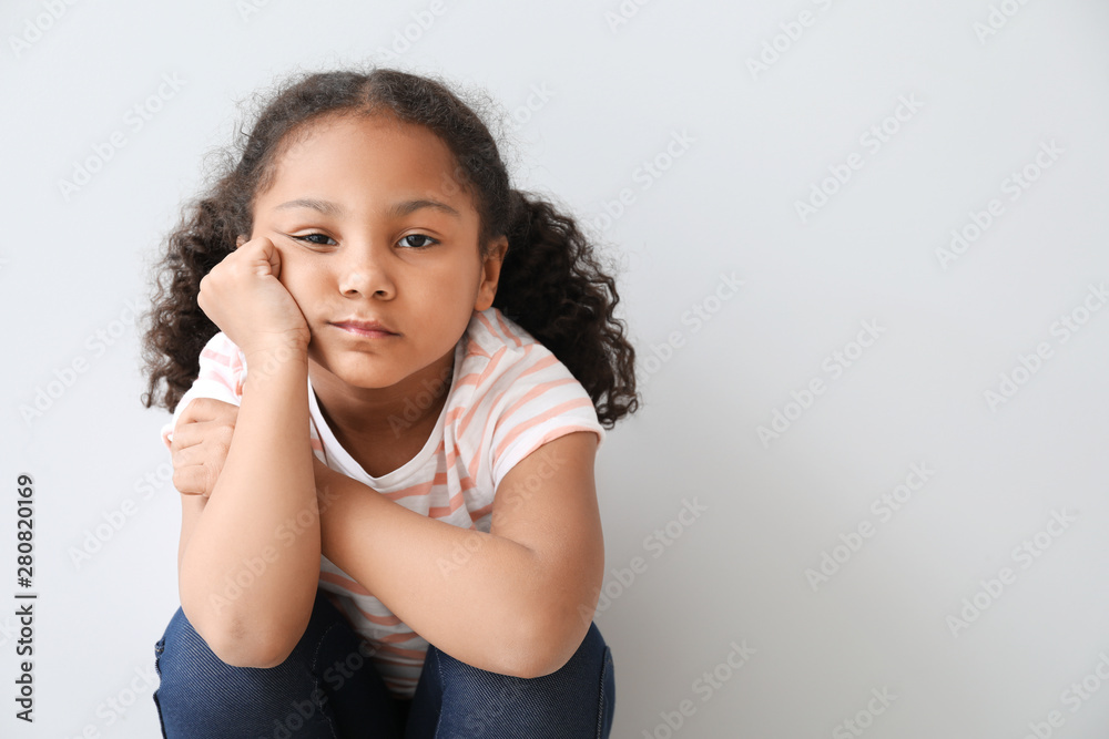 Portrait of sad little African-American girl on light background Portrait of sad little African-American girl on light background