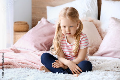 Sad little girl sitting on bed