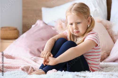 Sad little girl sitting on bed