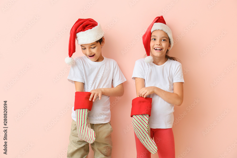 Happy little children in Santa hats and with Christmas stockings on color background - obrazy, fototapety, plakaty 