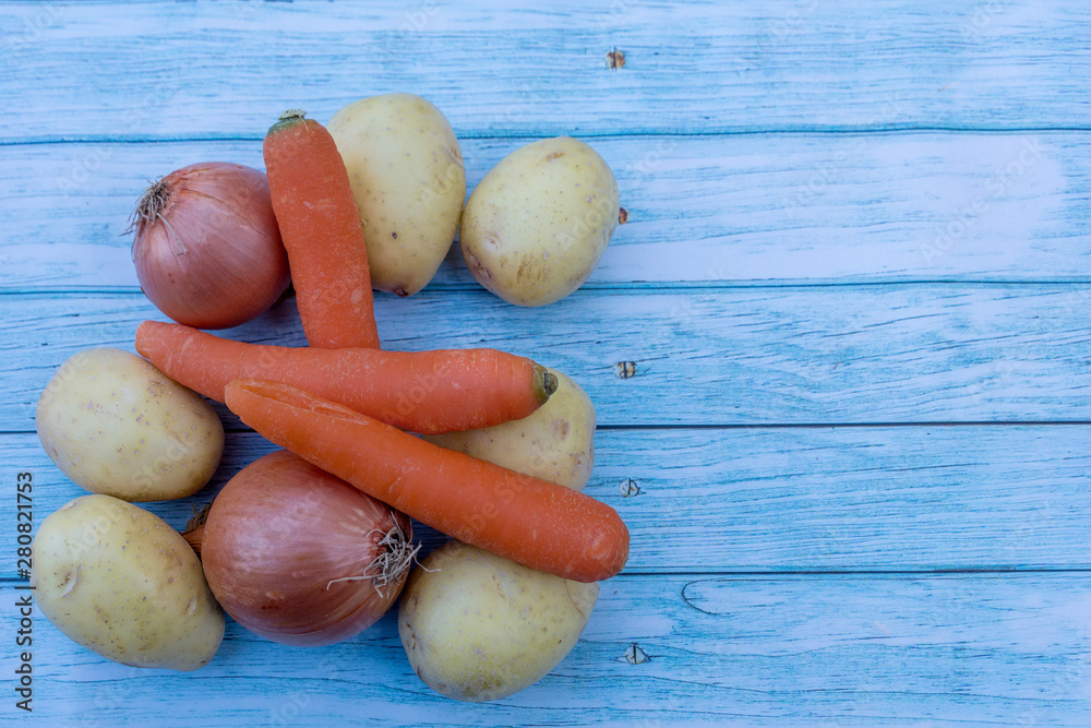 Potatoes, brown onions and carrots on a blue wooden table background. Cooking ingredients. Harvest. Potatoes, brown onions and carrots on a blue wooden table background. Cooking ingredients. Harvest.