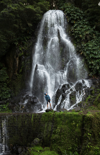 A man explores new, magical, and fantastic places around the world is in front of a waterfall, surrounded by nature and is looking upwards and relax. Sao Miguel island, Azores