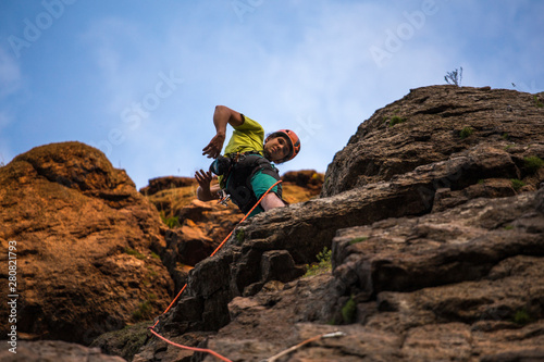 Low angle view of a man climbing on cliff against blue sky. Rope, helmet and all equipment.