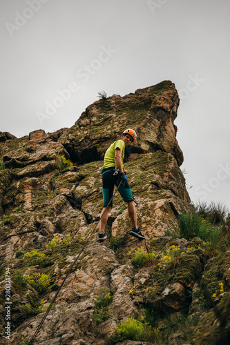 Low angle view of a man descending from the cliff against grey sky