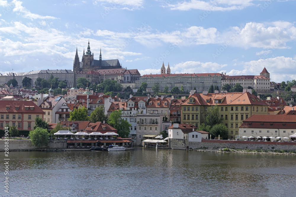 Prague, Czech Republic buildings, red roofs, and Prague Castle are shown looking west across the Vltava River during an afternoon day.