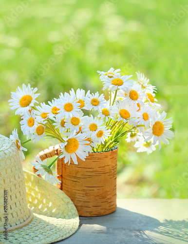 beautiful summer composition with chamomile flowers in Cup, braided hat in garden. Rural landscape background with Chamomile in sunlight. Summertime season. close up. soft selective focus