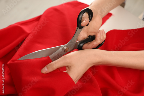 Woman cutting fabric with sharp scissors at white table, closeup