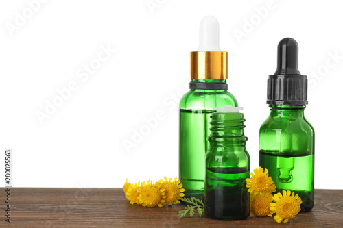 Bottles of herbal essential oils  pipette and flowers on wooden table  white background