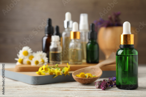 Bottles of different essential oils and wildflowers on wooden table, space for text