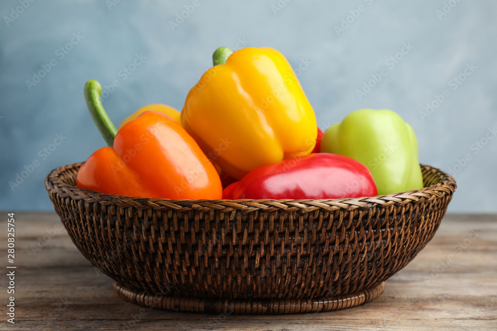 Wicker bowl with ripe bell peppers on wooden table against light blue background