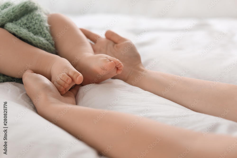 Mother holding feet of her little baby on bed, closeup Mother holding feet of her little baby on bed, closeup