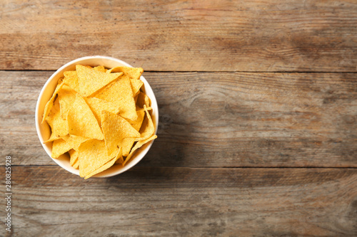 Tasty mexican nachos chips in bowl on wooden table, top view. Space for text
