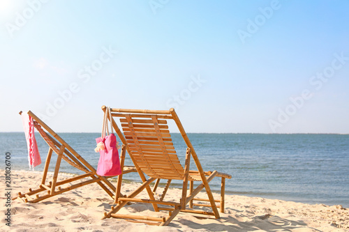 Empty wooden sunbeds and beach accessories on sandy shore