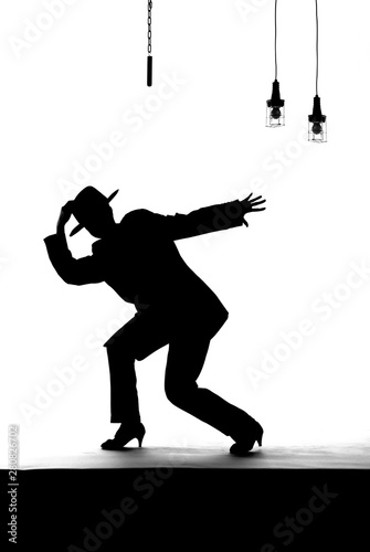 A female dancer dances on an old worn out stage. Dressed in men's clothing, she is seen dancing as a silhouette.