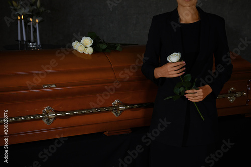 Young woman with white rose near casket in funeral home, closeup