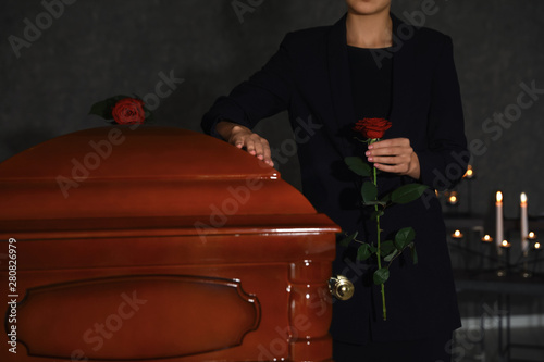 Young woman with red rose near casket in funeral home, closeup