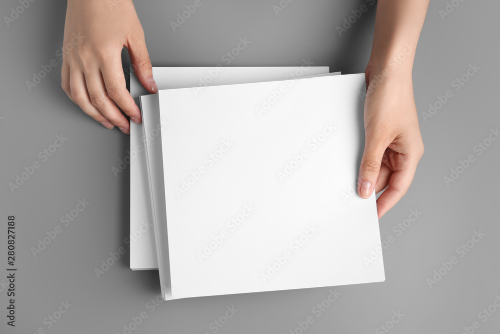 Woman holding blank paper sheets for brochure at grey table, top view. Mock up Woman holding blank paper sheets for brochure at grey table, top view. Mock up