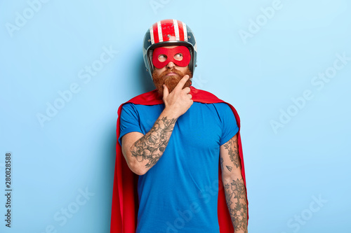 Konstfotografi Contemplative young bearded man with tattooed arms, thinks about flight, wears h