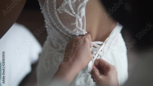 Bridesmaid wearing by hands and lacing the beautiful white wedding dress at the early morning. Woman support the cute and luxury bride. Dressing up for marriage.