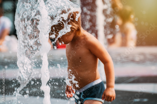 Fototapeta Naklejka Na Ścianę i Meble -  The child plays in the fountain in the hot summer