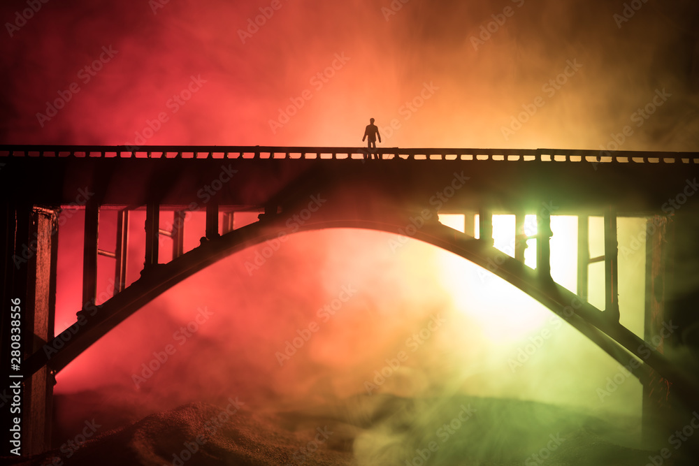 Obraz premium Artwork decoration. Silhouette of powerful metallic bridge at night with foggy backlight. Silhouette of person standing on bridge.