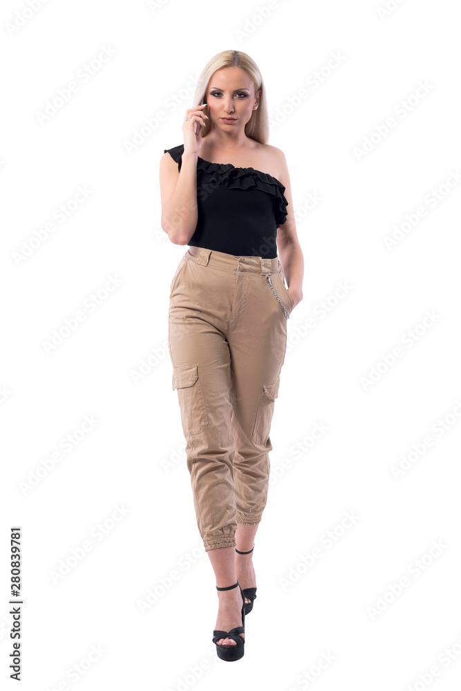 Sexy blonde stylish woman with attitude walking and talking on phone looking at camera. Full body isolated on white background. Sexy blonde stylish woman with attitude walking and talking on phone looking at camera. Full body isolated on white background.