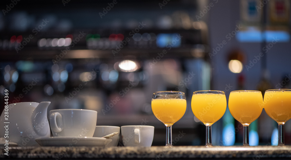 Glasses of orange juice, a teapot and two coffee cups on a bar counter Glasses of orange juice, a teapot and two coffee cups on a bar counter