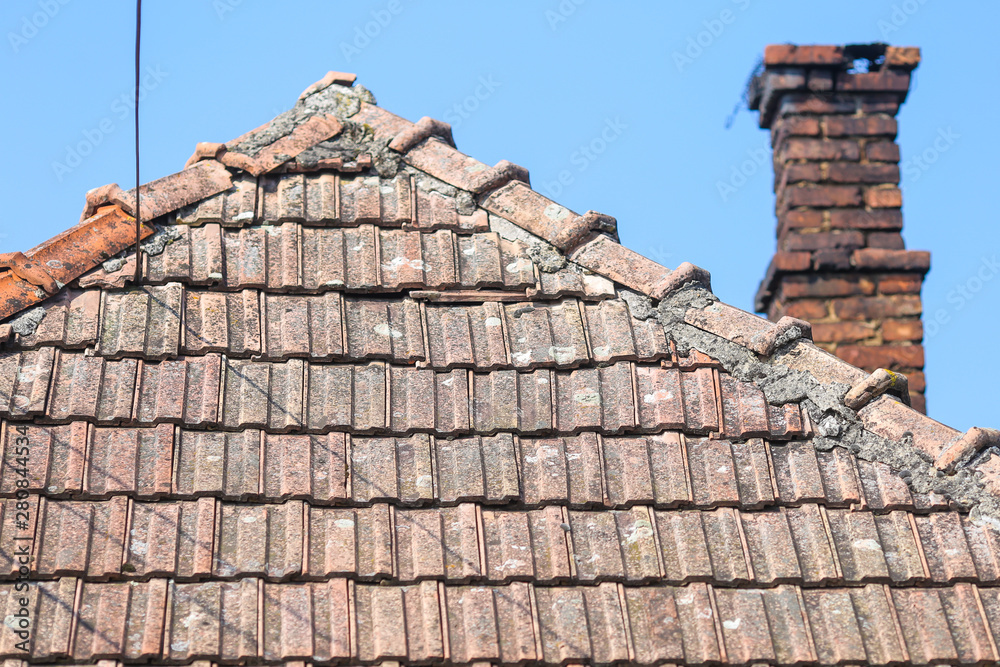 Details with the old ceramic roof tiles and with the red brick chimney of a house in a village in rural Romania