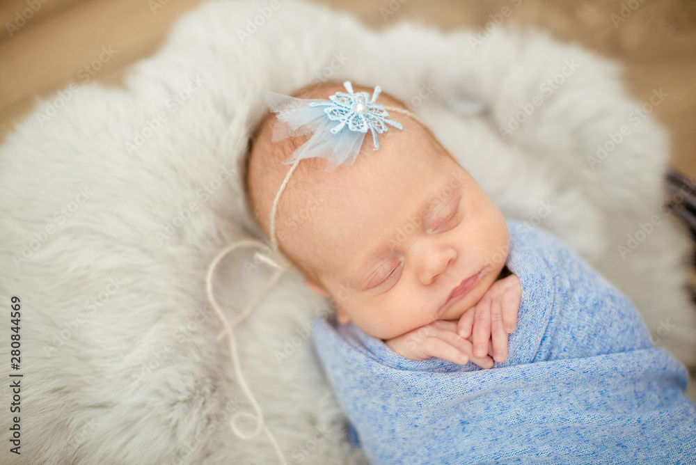 Perfect newborn baby girl in blue blanket in a wicker basket decorated with branches of spring cherry blossoms - obrazy, fototapety, plakaty 