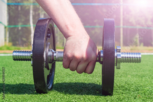 Dumbbell closeup lying on the grass. A man's hand holds it. Concept of sports in the open air, amateur sports, physical education. Place for text.