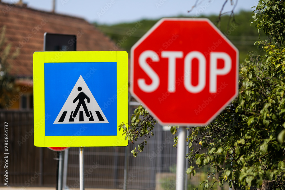Stop and pedestrian crossing sign one next to another on a street