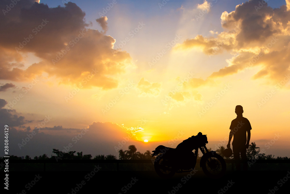 Silhouette of Back biker or rider,motorbike parking with sunset background .Traveller man standing and holding helmet beside motorcycle.Trip and lifestyle of motorbike concept,copy space.