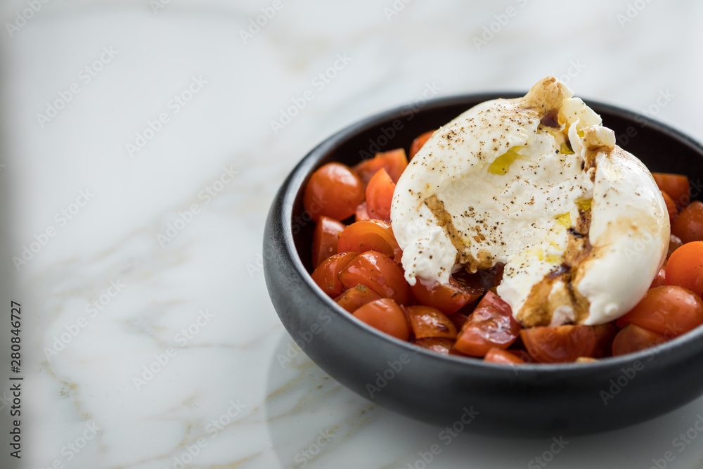 Burrata Büffelmozzarella Kugel mit Tomaten, Olivenöl und Balsamico auf schwarzen Teller