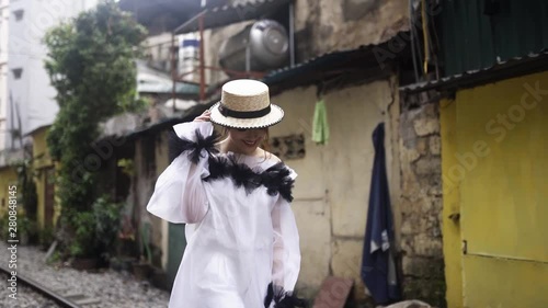 Beautiful and young fashion mestizo girl walking along the asian street with railway between old buildings. Journey concept in Vietnamese tourist destination. Cute female in white fashionable dress.