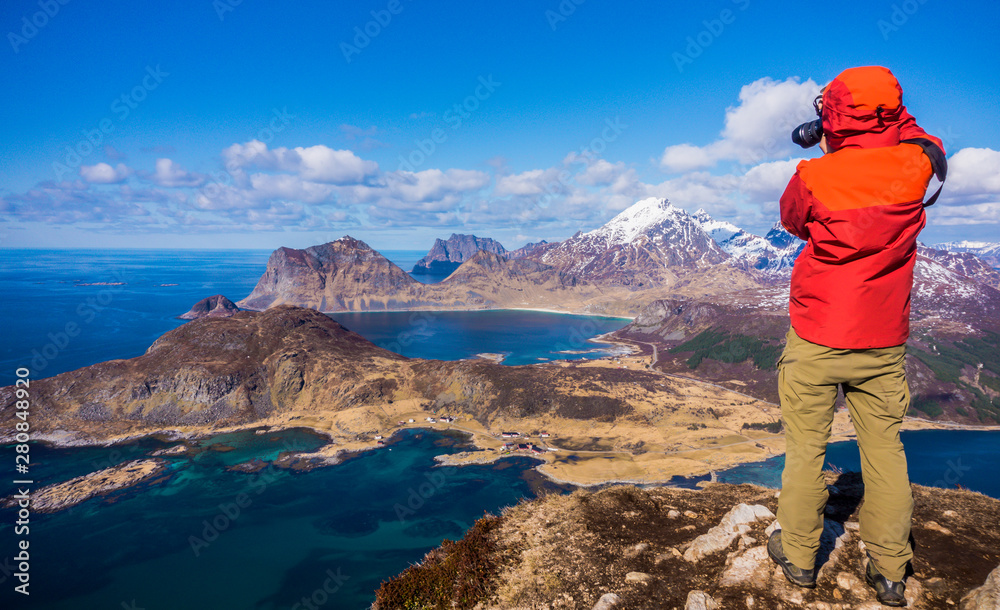 Offersoykammen Hiking Trail, Vestvagoy, Lofoten Islands, Norway. Top view from the peak of the mountain. Man taking photo of panorama view of fjords with blue water