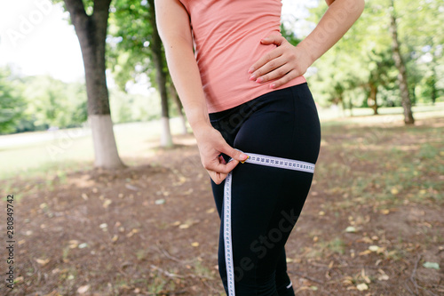 Weight loss, active lifestyle, sport and motivation. Fit woman in activewear measuring her hip with tape.