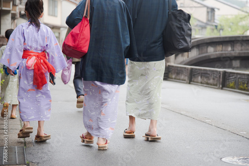 Japanese family wearing yukata or kimono and walking at Kinosaki Onsen village street in Toyooka City, Hyogo, Japan. See from back side in morning. Japan traveler trip. photo