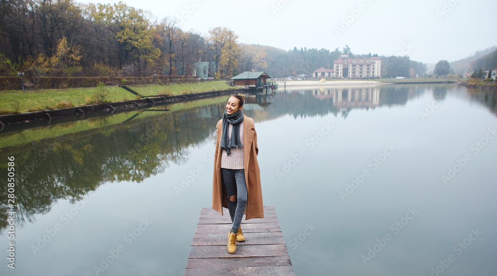 Fototapeta premium Happy woman walking on the wooden pier in the park at autumn.